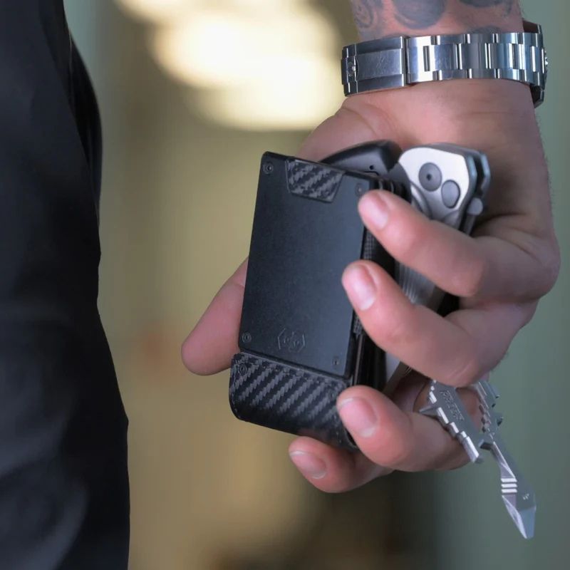 Hand holding a black proof wallet and silver multitool with blurred background