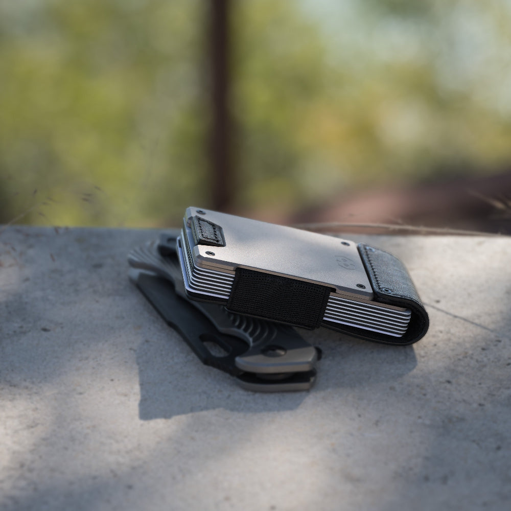 proof wallet with gunmetal backing laying on top of a tactical knife in an outdoor setting