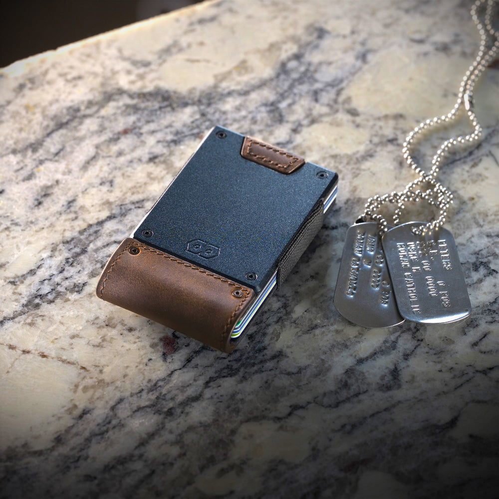 brown leather proof wallet with gunmetal backing sitting next to dog tags on a marble table