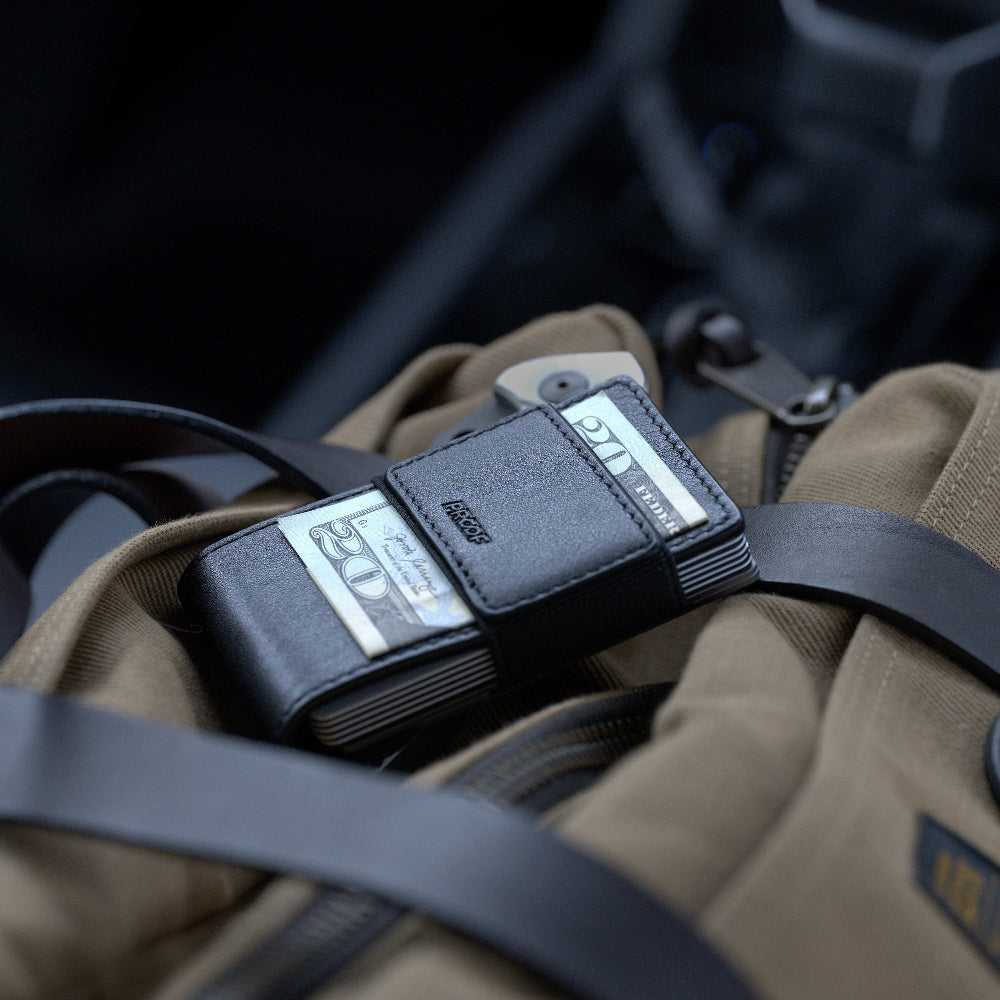 Close-up of a black leather proof wallet with visible brand name on a brown leather bag.
